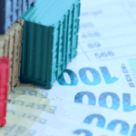 Abgebildet sind bunte Mini-Container, 100-Euro-Scheine und ein Stift auf einer Tabelle im Kontext von Pflichtangaben Rechnung