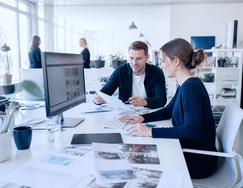 Zwei Mitarbeitende besprechen Projektaufgaben am Arbeitsplatz.