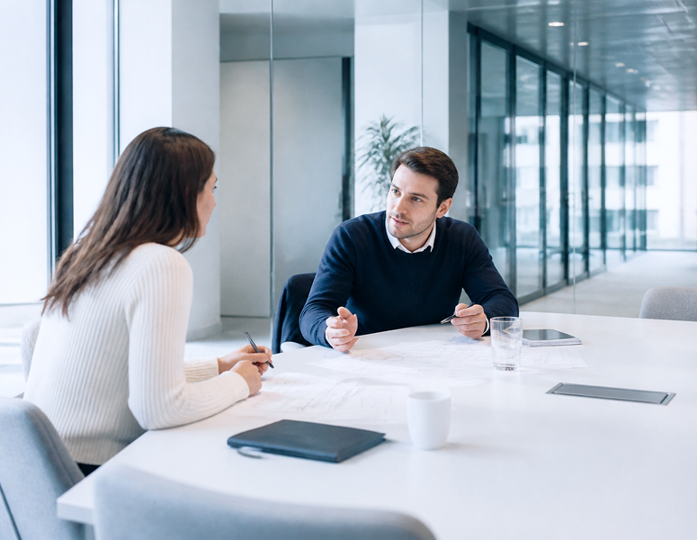 Berater und Kunde besprechen Unterlagen an einem Tisch zur Planung und Leistungserfassung eines Projekts.