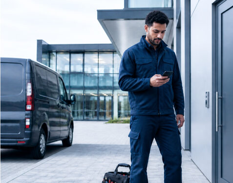 Servicetechniker nutzt sein Smartphone vor einem Firmengebäude für die mobile Projektzeiterfassung.