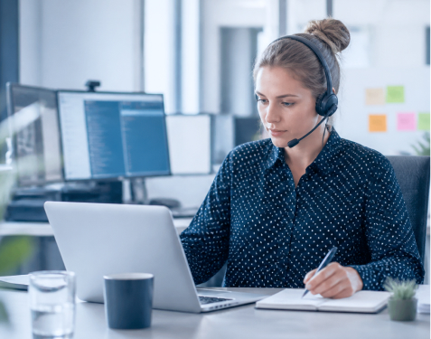 Supportmitarbeiterin mit Headset arbeitet am Laptop und notiert Informationen zu einer Kundenanfrage.