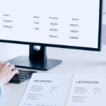 Mitarbeiterin arbeitet mit einer Abrechnungssoftware, während Rechnung, Lieferschein, Auftrag und Angebot auf dem Schreibtisch liegen.
